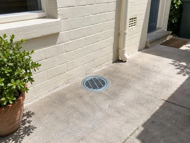 Dry paved side yard with a circular drain grate beside a brick wall and doorway in Coogee