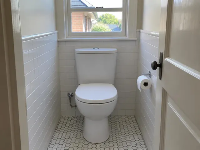 Clean white toilet in a small tiled bathroom with window light in Waverley