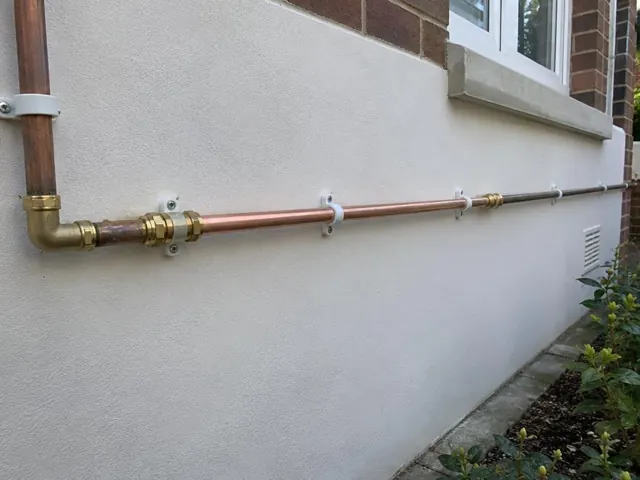 Repaired copper water pipe running along an exterior rendered wall with brick and window trim in Dover Heights